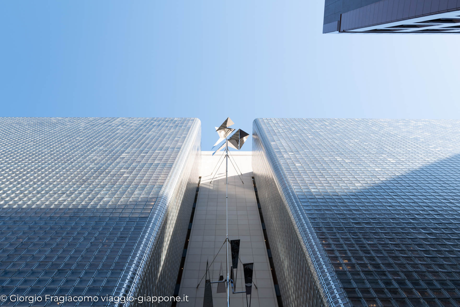 Veduta dal basso di un moderno grattacielo giapponese, con un'installazione artistica in cima.