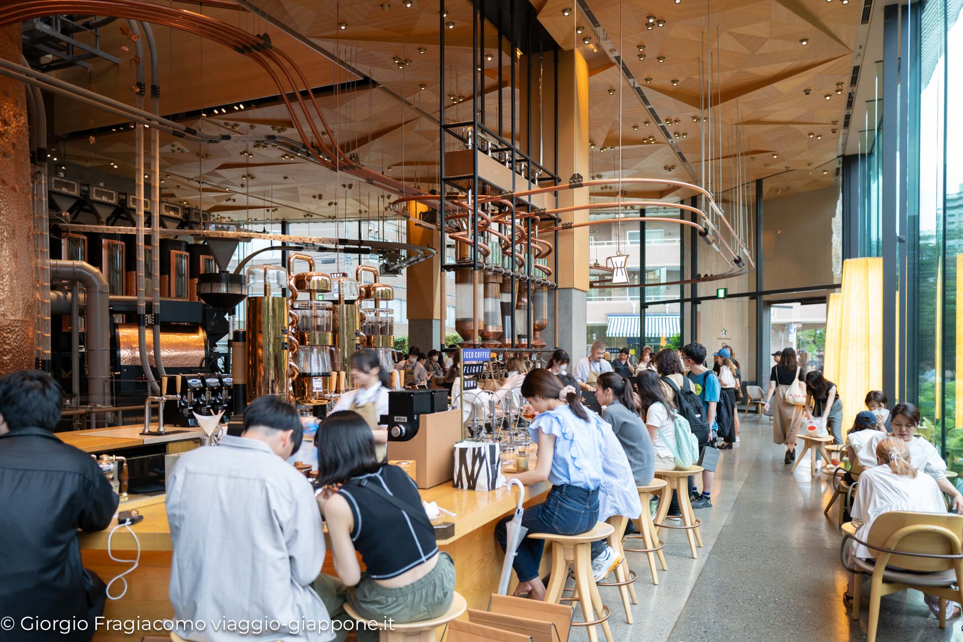 Interno di un caffè moderno in Giappone, con clienti che gustano bevande e osservano la preparazione del caffè.