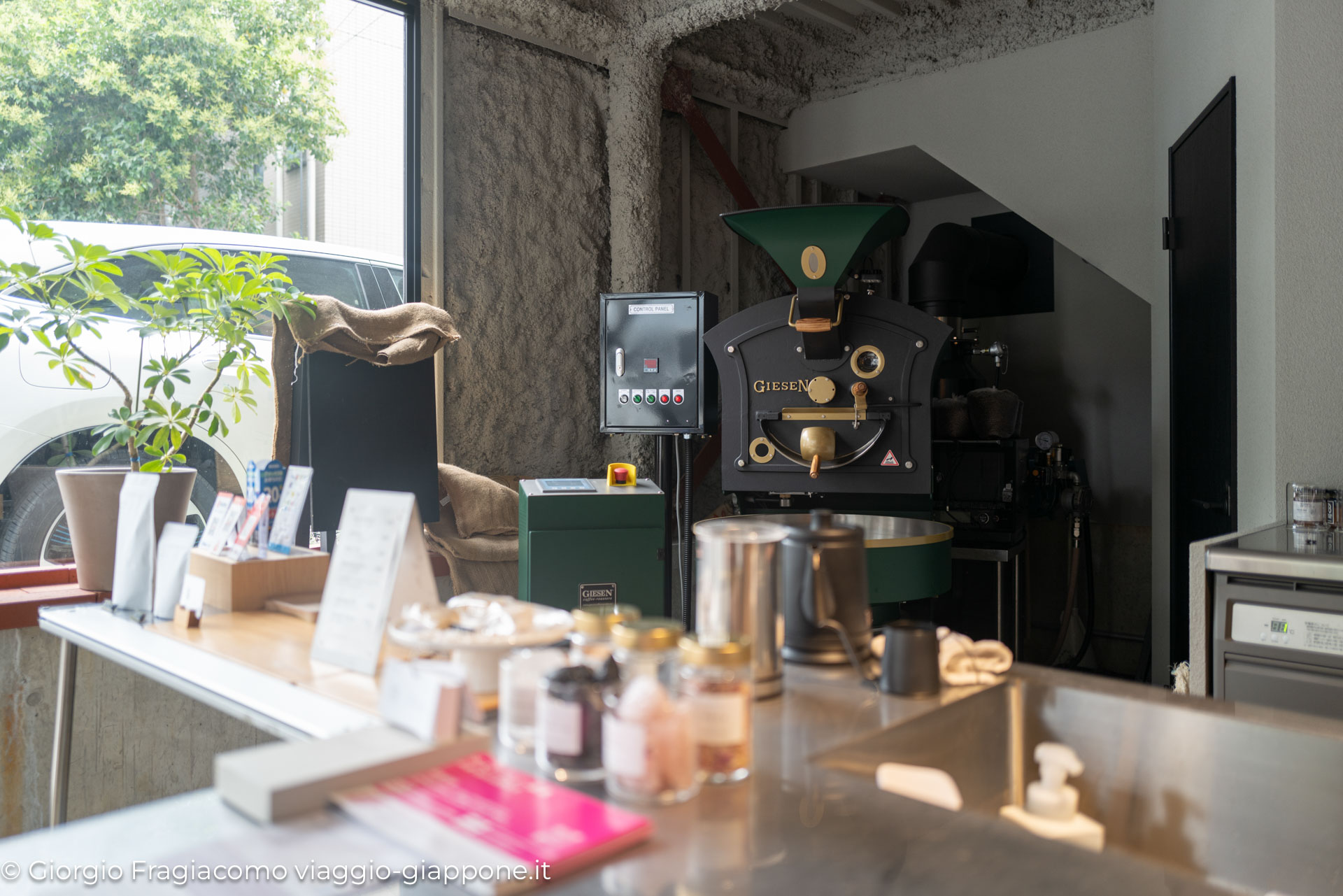 Interno di un caffè giapponese con torrefattrice Giesen, piante e accessori per la preparazione del caffè.