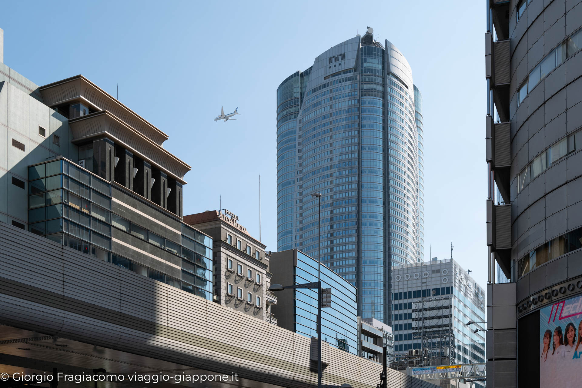 Vista di grattacieli moderni a Tokyo, con un aereo che sorvola il cielo sereno. Architettura giapponese contemporanea.